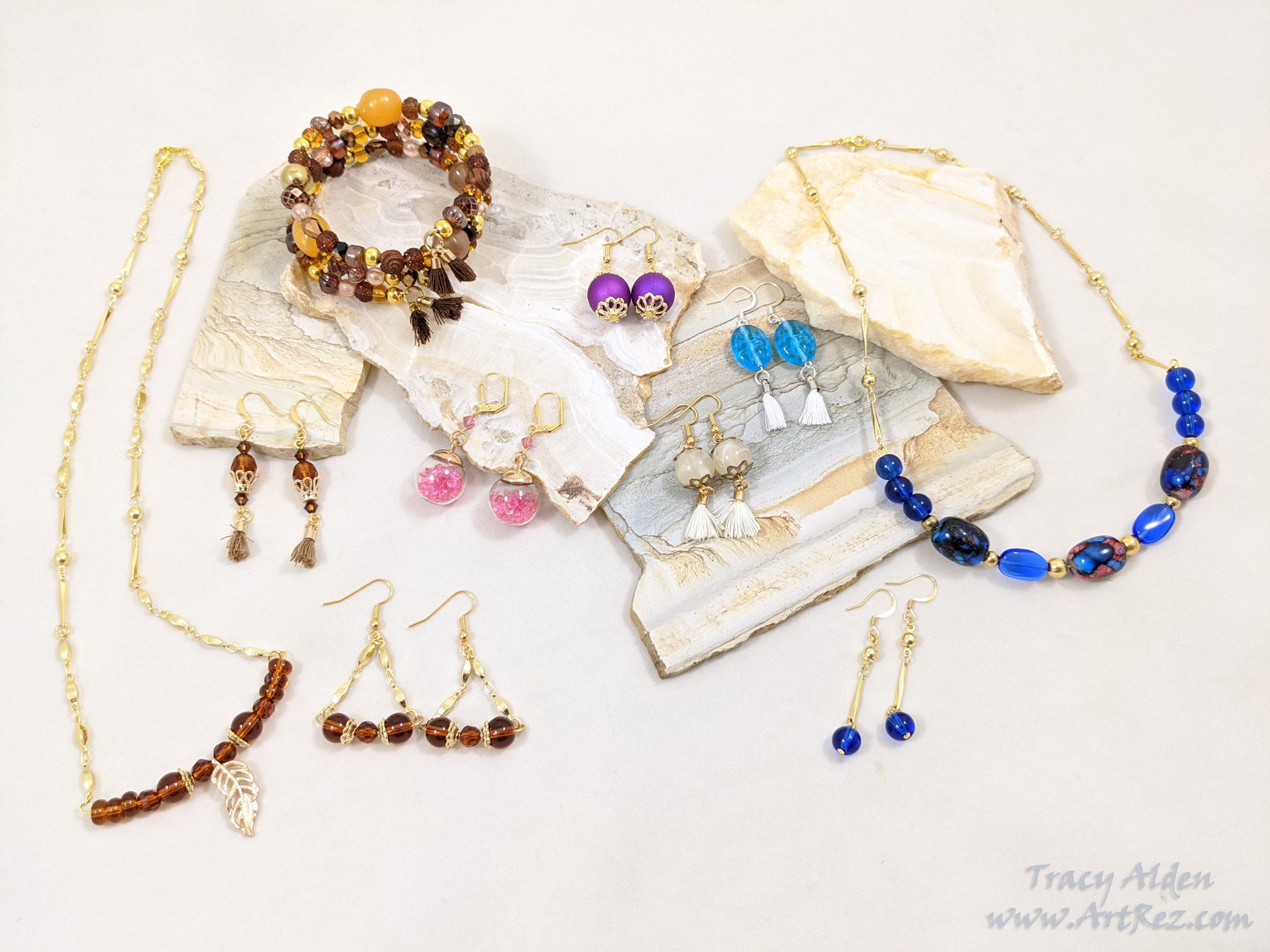 A mixed assortment of jewelry using gold tone mixed with brown, blue, purple and pink Jesse James Beads